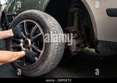 Autoreparaturen. Ersetzen der Räder. Saisonaler Reifenwechsel. Der Master entfernt das Rad mit beiden Händen mit dem Schlüssel. Ein Meister in Uniform Stockfoto