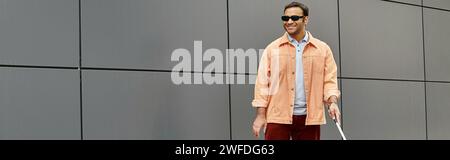 Fröhlicher indischer Blinder in Jacke mit Gehstock und Brille mit grauer Wand im Hintergrund, Banner Stockfoto