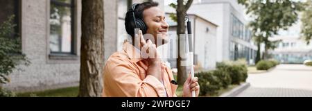 Fröhlicher behinderter indischer Mann in legeren Kleidern mit Kopfhörern und Gehstock, der Musik und Banner genießt Stockfoto