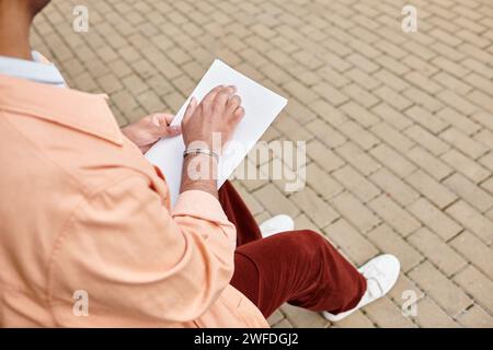 Zugeschnittener indischer Behinderter im Jackett, der auf der Bank sitzt und blindenschrift liest, blind Stockfoto