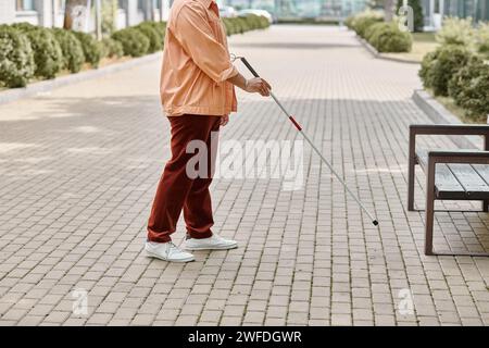 Zugeschnittene Ansicht eines blinden indianers in orangefarbener Jacke mit Gehstock im Freien Stockfoto