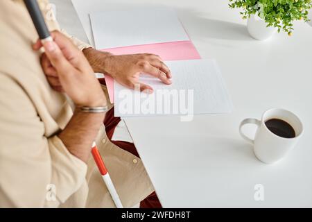 Zugeschnittene Ansicht eines indischen Blinden in alltagstauglicher, gemütlicher Kleidung mit Wanderstock, der brailleschrift liest Stockfoto