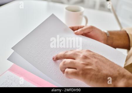 Zugeschnittene Ansicht eines indianischen Blinden in Freizeitkleidung mit Gehstock und Kaffee, der brailleschrift liest Stockfoto