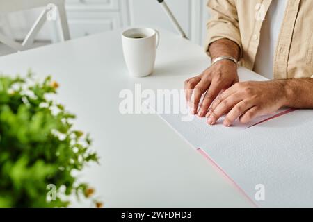 Zugeschnittene Ansicht eines indianischen Blinden in gemütlicher Kleidung, der am Tisch sitzt und blindenschrift liest, behindert Stockfoto