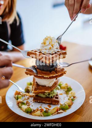 Waffeln, Gaufre oder Wafel oder Waffeln mit Obst, Eis und Belag. Süßer Genuss. Frisch gebackene Eiswaffel mit köstlichen Toppings auf Holz Stockfoto