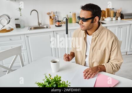 Hübscher indischer Blinder in gemütlicher Kleidung mit Brille und Gehstock, der brailleschrift liest Stockfoto