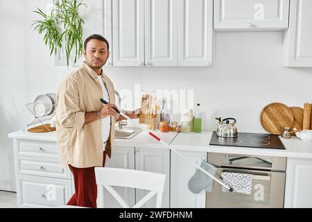 Attraktiver indischer Mann mit Blindheit in lässiger Kleidung, der in der Küche ein Glas Makkaroni pflückt Stockfoto