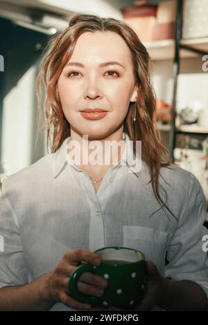 Lächelnde Brünette mittleren Alters mit einer Tasse Tee im Sonnenlicht Stockfoto