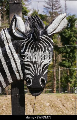 Equus burchellii - Zebraskulptur, die an einem Holzpfosten auf einem Tiergehege befestigt ist. Stockfoto