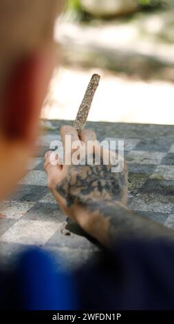 Eine tätowierte Hand, die einen Marihuana-Blunt im Outdoor-Park hält Stockfoto