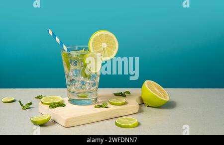 Cocktail in Glas gefüllt mit Eis und Zitronenscheiben garniert mit Zitronenscheiben und Sorbet auf einem Holzbrett vor türkisfarbenem Hintergrund Stockfoto