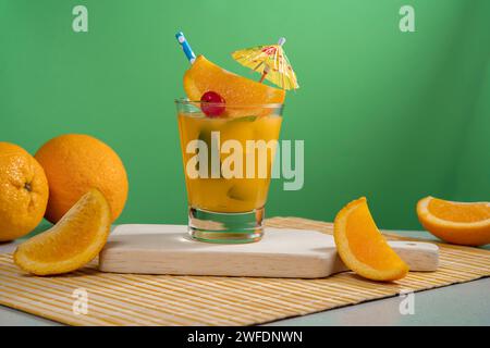 Gelber Cocktail in Glas gefüllt mit Eis und Minzblättern garniert mit Orangenscheibe, Kirsche, Sorbet und gelbem Schirm auf einer Bambusserviette mit Stockfoto
