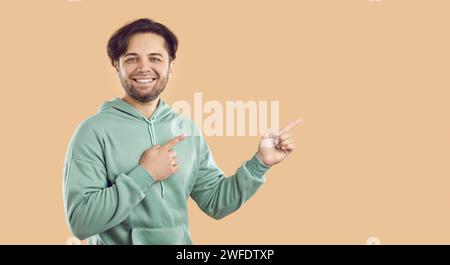 Glücklicher Mann, der den Verkauf von Freizeitmoden angibt und auf den Kopierraum auf beigefarbenem Hintergrund zeigt Stockfoto
