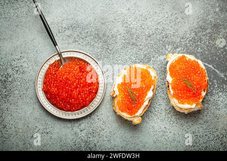 Kleine Metallplatte mit rotem Lachskaviar und zwei Kaviar Toast Canapé auf grauem Betonhintergrund, festliche Luxus Delikatesse und Vorspeise Stockfoto