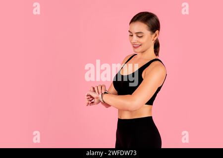 Lächelnde sportliche Frau in Sportbekleidung, die ihre Smartwatch überprüft Stockfoto