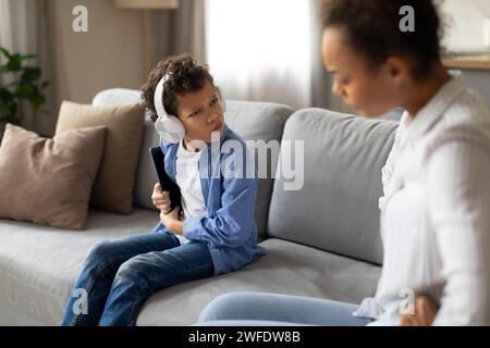 Junger schwarzer Junge mit Kopfhörern in Uneinigkeit mit Mutter Stockfoto