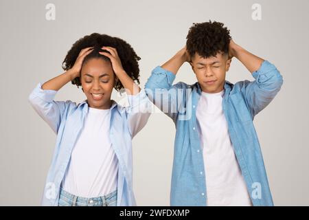 Gestresste afroamerikanische junge Frau und Mann mit Händen auf dem Kopf, Augen geschlossen Stockfoto