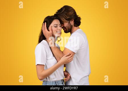 Intime Paare in weißen T-Shirts teilen einen zärtlichen Moment, während der Mann sanft das Gesicht der Frau wiegt Stockfoto