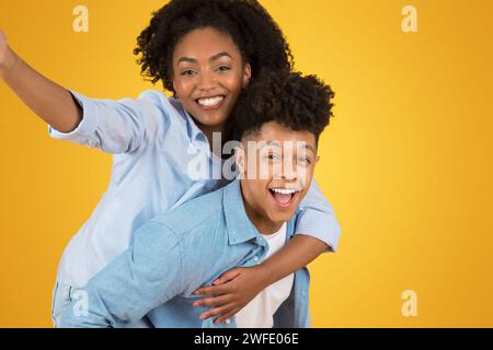 Überschwängliche junge Frau mit weit geöffneten Armen, die Huckepack auf einem entzückten jungen Mann reitet Stockfoto