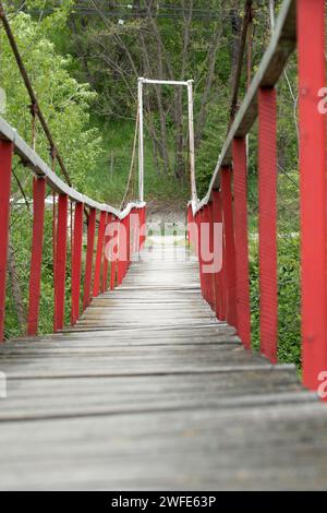 Eine hölzerne Fußgängerbrücke mit roten Geländern, die einen Fluss überquert. Stockfoto
