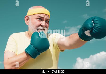 Schöner älterer Mann, der Boxtritte übt. Ein älterer Mann schlägt einen Boxsack. Ältere Männer kämpfen gegen Posen. Senior Sportmann mit Boxhandschuhen. Stockfoto