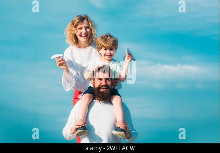 Familienreise und Urlaubskonzept. Vater trägt seinen Sohn auf den Schultern. Elternschaft und Kindheitskonzept. Kinder, die mit einfachen Papierflugzeugen spielen Stockfoto