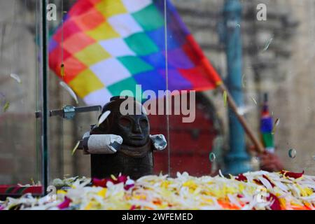 La Paz, BOLIVIEN; 24. Januar 2015. Eine antike illa (oder Statue) eines Ekeko (ein Gott des Überflusses der Aymara) vor der Kirche von San Francisco und eine Wiphala-Flagge, die durch die Straßen von La Paz geführt wird, um ihren ersten Auftritt beim Alasitas-Festival zu feiern, das heute beginnt. Die Statue ist etwa 2000 Jahre alt und wurde von der Pucara-Kultur hergestellt. Sie wurde 1858 von der archäologischen Stätte Tiwanaku in die Schweiz gebracht und im November 2014 vom Geschichtsmuseum Bern nach Bolivien zurückgegeben. Stockfoto