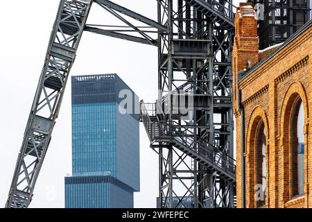 Ein Bergwerksschacht gegen einen bewölkten Himmel. Moderne Bürohochhäuser im Hintergrund, alte Backsteinhäuser im Vordergrund Stockfoto