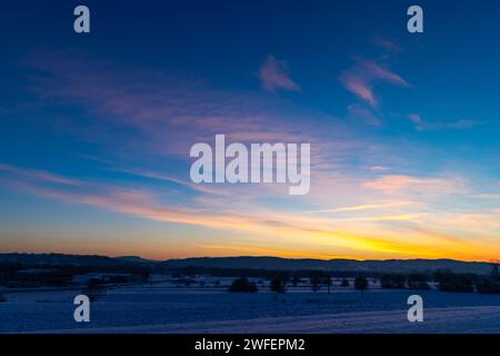 Die Sonne geht über schneebedeckten Feldern auf. Ein goldenes Leuchten am Horizont. Kalter und frostiger Morgen des Wintertages Stockfoto