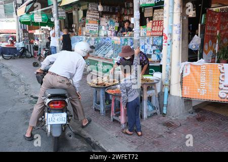 Man o n Roller hält an, um bei einem Straßenverkäufer in der Innenstadt von Phnom Penh, Kambodscha, zu kaufen Stockfoto