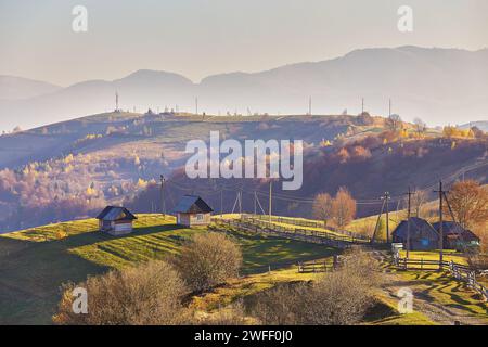 Panoramablick auf den nebelig sonnigen Herbstabend in den Bergen. Wunderschöne Landschaft bei Sonnenuntergang. Hänge, Wiesen, Felder, Dorf, Haus, unbefestigte Straße. Amazi Stockfoto