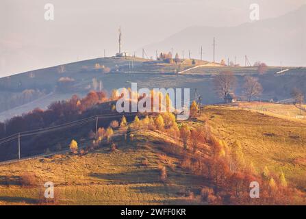 Panoramablick auf den nebelig sonnigen Herbstabend in den Bergen. Wunderschöne Landschaft bei Sonnenuntergang. Hänge, Wiesen, Felder, Dorf, Haus, unbefestigte Straße. Amazi Stockfoto