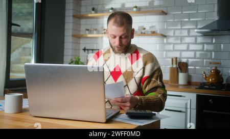 Erwachsener Mann, der in der Küche sitzt mit Tablet-Computer Rechnungen bezahlen, Taschenrechner Ausgaben zählen, Budgetkontrolle vornehmen, Finanzen verwalten, überfällige Darlehen prüfen Stockfoto