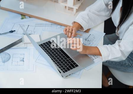 Professioneller, schöner Ingenieur mit Laptop-Analyse-Blueprint mit architektonischem Dokument und Hausmodell auf dem Tisch. Kreatives Business-Design Stockfoto