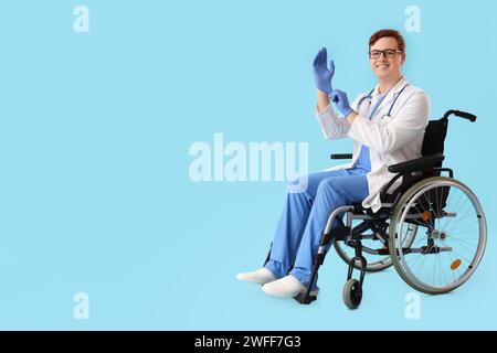 Männlicher Arzt im Rollstuhl, der medizinische Handschuhe auf blauem Hintergrund trägt Stockfoto