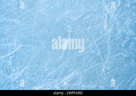 Eisiger Hintergrund auf der Eisbahn mit sichtbaren Spuren des Skatings, die das Wesen des Wintersports zeigen. Die Struktur des Eises auf der Eislaufbahn ist von oben sichtbar und zeigt eine zerkratzte Eisschicht. Stockfoto