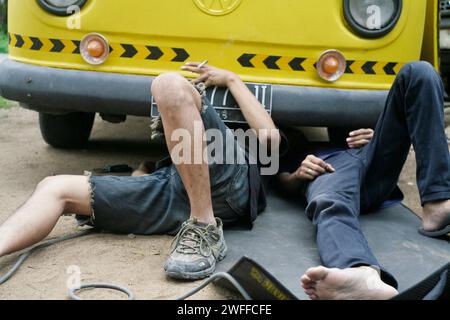 Ein junger Mann, der ein Lenkproblem an einem alten Auto repariert, unter dem Auto schweißt. Stockfoto