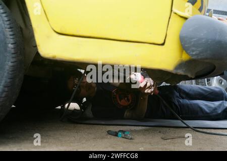 Ein junger Mann, der ein Lenkproblem an einem alten Auto repariert, unter dem Auto schweißt. Stockfoto