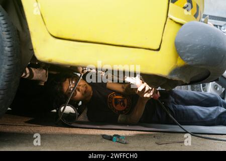 Ein junger Mann, der ein Lenkproblem an einem alten Auto repariert, unter dem Auto schweißt. Stockfoto