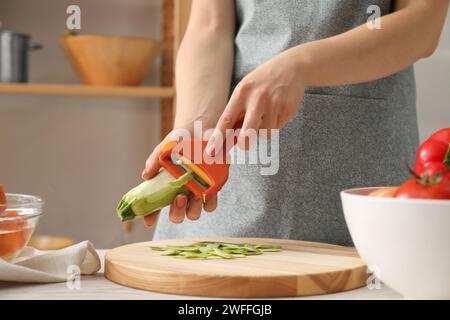 Frau, die frische Zucchini am Tisch in der Küche schält, Nahaufnahme Stockfoto