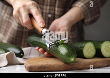 Frau, die frische Gurke am weißen Holztisch schält, Nahaufnahme Stockfoto