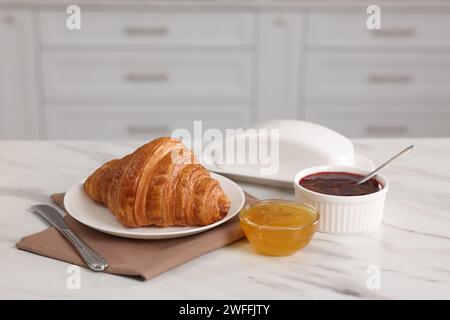 Frühstückszeit. Frisches Croissant, Marmelade und Honig auf weißem Tisch Stockfoto