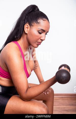 Junge Fitnessfrau, in Turnkleidung gekleidet, sitzend und mit Kurzhanteln Armübungen gemacht. Gesundes Leben mit körperlicher Bewegung. Stockfoto