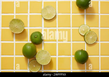 Die minimalen Szenen mehrerer Limetten- und Limettenscheiben sind auf gelbem Mosaikhintergrund dekoriert. Leerraum für kosmetische Präparate von Kalk ( Stockfoto