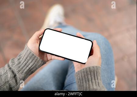 Ein Nahbild eines Smartphones mit weißem Bildschirm in horizontaler Position in der Hand einer Frau mit verschwommenem Hintergrund. Menschen und kabellose Technologie Stockfoto