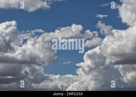 Himmel gefüllt mit großen, geschwollenen Wolken, die sich über den Horizont erstrecken, wenige der Wolken werden von der hellen Sonne beleuchtet und werfen ein weiches goldenes Licht über den Horizont Stockfoto