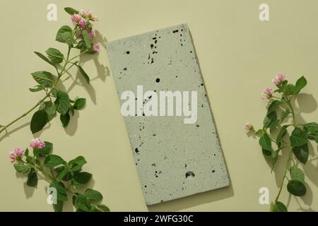 Ein leeres Podium aus Stein in grauer Farbe, dekoriert mit einigen Lantana Camara Blumen auf hellem Hintergrund. Leerzeichen für Produktwerbung. Natürliche Konnektivität Stockfoto