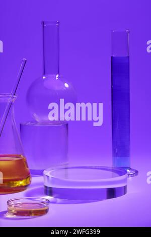 Messzylinder aus blauer Flüssigkeit, konischer Kolben und Petrischale aus orangener Flüssigkeit, angeordnet mit einem runden, transparenten Podium. Laborkonzept Stockfoto