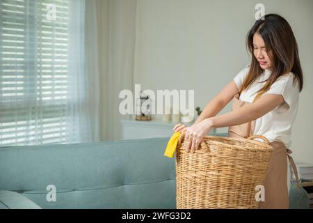 Eine asiatische Hausfrau hielt einen Korb mit verschiedenen Kleidern auf dem Sofa im Wohnzimmer Stockfoto