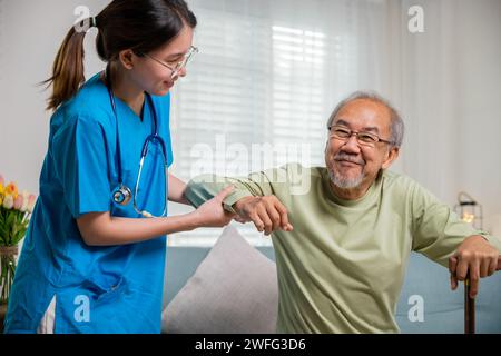 Pflegende Krankenschwester hilft älteren Behinderten beim Aufstehen mit Gehstock Stockfoto